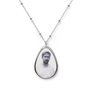 May include: A silver chain necklace with a teardrop-shaped pendant featuring a black and white photo of a man.