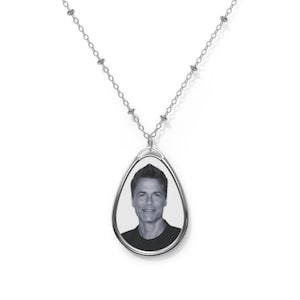 May include: A silver chain necklace with a teardrop-shaped pendant featuring a black and white photograph of a man.