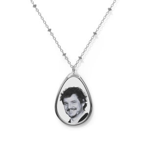 Puede incluir: Un collar de cadena de plata con un colgante en forma de lágrima que presenta una foto en blanco y negro de un hombre.