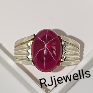 Peut inclure: Bague en argent ornée d'une grande pierre précieuse ovale rouge foncé. La pierre présente un motif en forme d'étoile. La bague a un anneau en argent avec un motif texturé. Le texte "RJjewells" est visible.