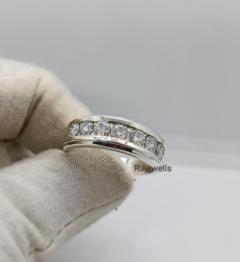 May include: A silver ring with a row of seven clear, round-cut stones. The ring has a polished finish and a wide band. The text "RJjewells" is visible on the side of the ring.
