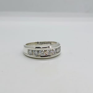 May include: A silver ring with a row of clear, round gemstones set across the top. The ring has a polished finish and the text "RJewells" is visible on the side. The ring is set against a plain white background.