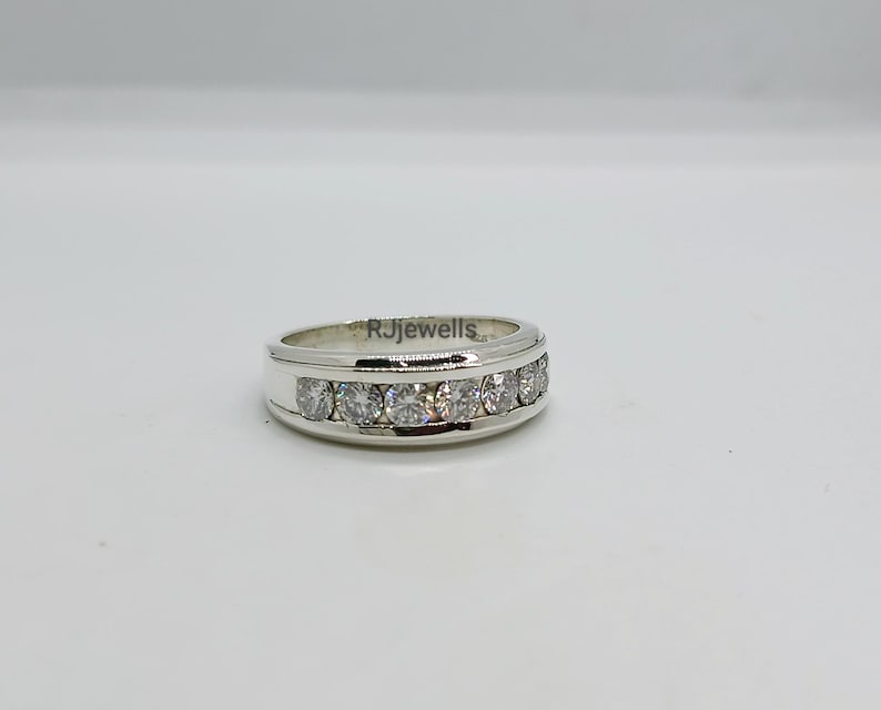 May include: A silver ring with a row of clear, round gemstones set across the top. The ring has a polished finish and the text "RJewells" is visible on the side. The ring is set against a plain white background.