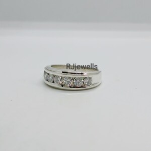 May include: A silver ring with a row of six clear gemstones. The ring has a polished finish and is set against a white background. The text "Rjjewells" is visible on the ring.