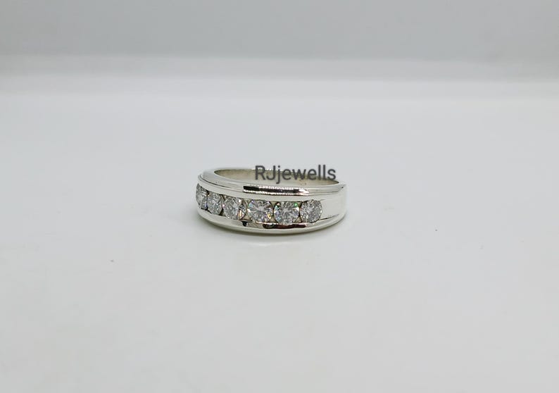 May include: A silver ring with a row of six clear gemstones. The ring has a polished finish and is set against a white background. The text "Rjjewells" is visible on the ring.