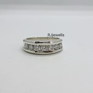 May include: A silver ring with a row of clear, round gemstones set across the top. The ring has a polished finish and is displayed on a white surface. The text "RJjewells" is visible on the image.