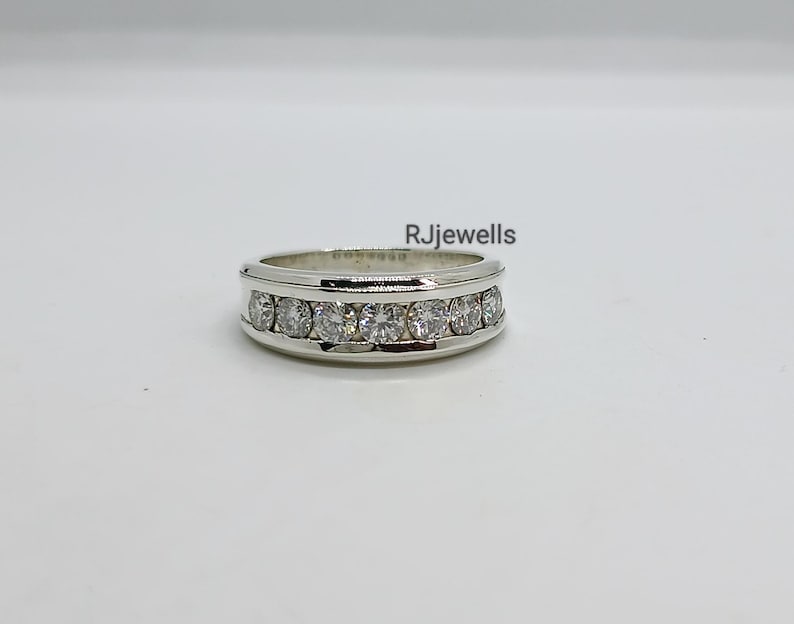 May include: A silver ring with a row of clear, round gemstones set across the top. The ring has a polished finish and is displayed on a white surface. The text "RJjewells" is visible on the image.