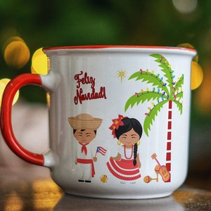May include: White ceramic mug with a red handle. The mug features a festive Christmas scene with a palm tree decorated with lights, a man and a woman in traditional clothing, and the text "Feliz Navidad".