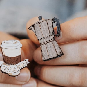 Könnte beinhalten: Zwei Holz-Anstecknadeln, eine in Form einer Kaffeetasse mit dem Text "Coffee Lover" und die andere in Form einer Kaffeekanne.