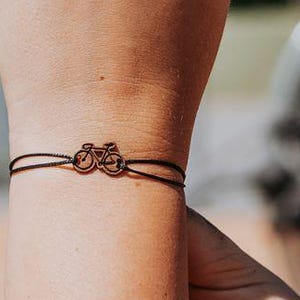 Puede incluir: Una pulsera negra con un pequeño dije de bicicleta plateado.