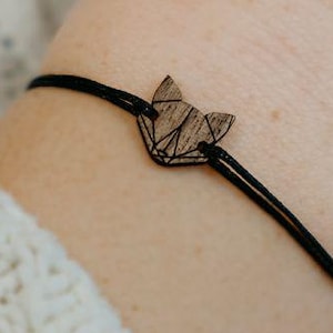 Könnte beinhalten: Ein schwarzes Armband aus Schnur mit einem Holz-Fuchs-Anhänger. Der Fuchs ist aus Holz und hat ein geometrisches Design.