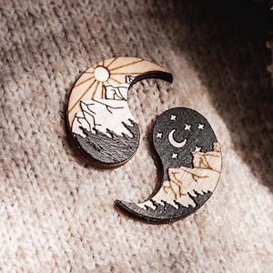 Könnte beinhalten: Ein hölzerner Yin-Yang-Pin mit einer Bergszene auf jeder Seite. Die linke Seite zeigt eine Sonne und eine Bergkette auf einem hellbraunen Hintergrund. Die rechte Seite zeigt einen Mond und eine Bergkette auf einem dunkelbraunen Hintergrund.