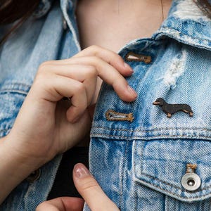 Könnte beinhalten: Eine schwarze Dackel-Holz-Anstecknadel auf einer blauen Jeansjacke.