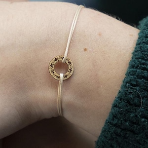 Könnte beinhalten: Ein schlichtes Armband mit einem runden Holzanhänger. Der Anhänger hat ein dekoratives, eingraviertes Design.