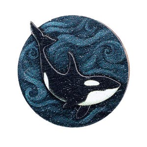 Könnte beinhalten: Ein runder, dunkelblauer Anstecker mit einem schwarz-weißen Orca-Wal-Design. Der Wal ist vor einem Hintergrund aus wirbelnden blauen Wellen platziert. Der Anstecker hat ein glänzendes, metallisches Finish.