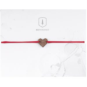 Könnte beinhalten: Ein rotes Armband mit einem Holzherz-Anhänger. Der Anhänger ist ein einfaches Herz mit natürlicher Holzmaserung. Das Armband liegt auf einem weißen Hintergrund mit dem darunter gedruckten Text "BEWOODEN".