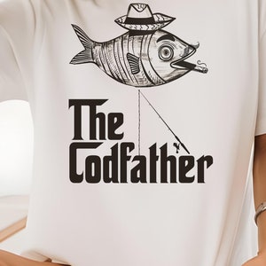 May include: White t-shirt with a graphic of a fish wearing a hat and holding a fishing rod. The text "The Codfather" is printed below the fish.