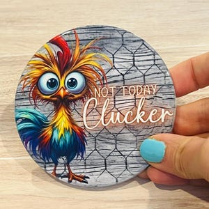 May include: A round coaster with a colorful cartoon rooster with big eyes and the text "Not Today Clucker" on a woodgrain background with a chicken wire pattern.