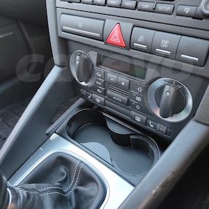 Può includere: Interni di un'auto con cruscotto nero. Sono visibili i comandi del climatizzatore, il pulsante delle luci di emergenza e uno schermo "Audi Navigation plus". Sono visibili anche la leva del cambio e i portabicchieri.