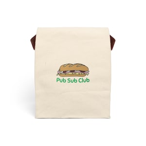 May include: A white canvas tote bag with brown handles. The bag features a green and brown illustration of a sub sandwich and the text "Pub Sub Club".
