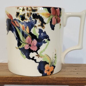 Pu&ograve; includere: Tazza in ceramica color crema con un disegno a mappa. La mappa &egrave; principalmente blu navy, con accenti dorati e illustrazioni floreali colorate. Il manico ha una forma angolare unica. Il bordo &egrave; rosa.