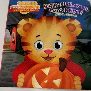 Peut inclure: Un livre pour enfants intitul&eacute; "Joyeux Halloween, Daniel Tiger !" pr&eacute;sente un tigre de dessin anim&eacute; tenant une citrouille orange. La couverture porte le texte "Daniel Tiger's Neighborhood" et "A Lift-the-Flap Book."
