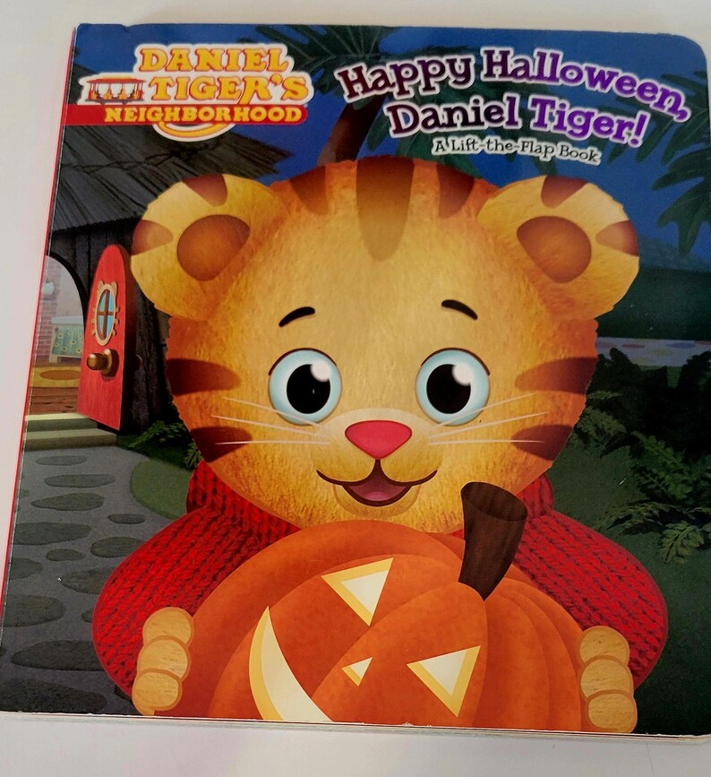 Peut inclure: Un livre pour enfants intitul&eacute; "Joyeux Halloween, Daniel Tiger !" pr&eacute;sente un tigre de dessin anim&eacute; tenant une citrouille orange. La couverture porte le texte "Daniel Tiger's Neighborhood" et "A Lift-the-Flap Book."