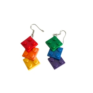 Puede incluir: Pendientes de Lego de color arcoíris. Cada pendiente tiene cuatro ladrillos apilados en los colores rojo, naranja, amarillo, verde, azul y morado.