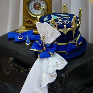 May include: A blue and gold crown-shaped hat with a white bow and a white fabric streamer. The hat is decorated with gold accents and blue jewels.