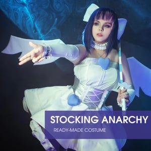 以下が含まれることがあります： ストッキングアナーキーの既製コスチューム。白いドレスは青いハートのアクセントとコルセットスタイルのボディスが特徴です。キャラクターは、ピンクのハイライトが入った青いウィッグ、白い手袋、お揃いのチョーカーを着用しています。青と白の剣が右手で保持されています。