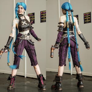 May include: A woman in a cosplay costume of Jinx from the video game League of Legends. She is wearing a purple and black striped pants, a brown leather top, and blue hair with pigtails. She is holding two guns in her hands.