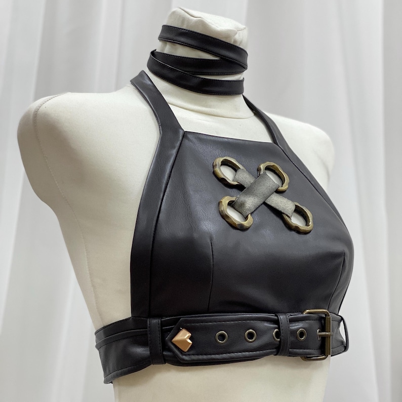 May include: A black leather halter top with a criss-cross design and gold-tone hardware. The top has a belt with a heart-shaped buckle.
