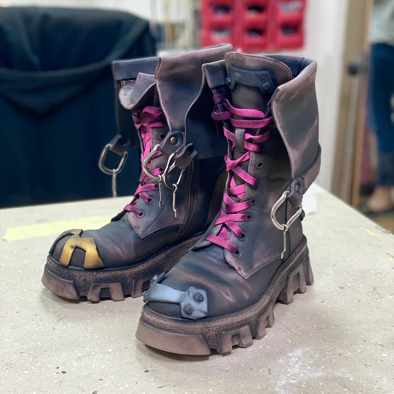 May include: A pair of black leather boots with pink laces and silver buckles. The boots have a distressed look and a chunky platform sole.