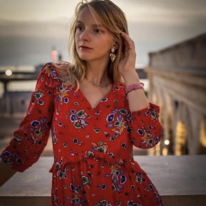 Peut inclure: Robe rouge à imprimé floral avec un col en V et des manches longues. La robe présente un motif de fleurs bleues, blanches et jaunes. La robe a une taille à volants et est faite d'un tissu léger.