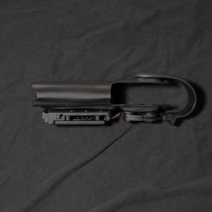 May include: A black plastic holster, designed for a firearm. It has a belt loop and a trigger guard. The object is set against a dark background.