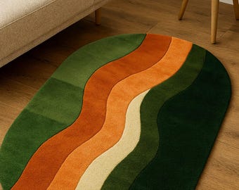 Puede incluir: Una alfombra ovalada con un diseño ondulado en tonos verdes, naranjas y beige. La alfombra está colocada sobre un suelo de madera, con un sofá beige y una pequeña mesa de madera en el fondo. Las dimensiones de la alfombra no son visibles.
