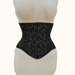May include: A black satin corset with a decorative design of black sequins.