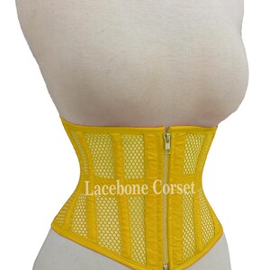 May include: A bright yellow corset with a mesh and vertical panel design. The corset has a front zipper closure and is displayed on a mannequin. The text "Lacebone Corset" is visible on the front.