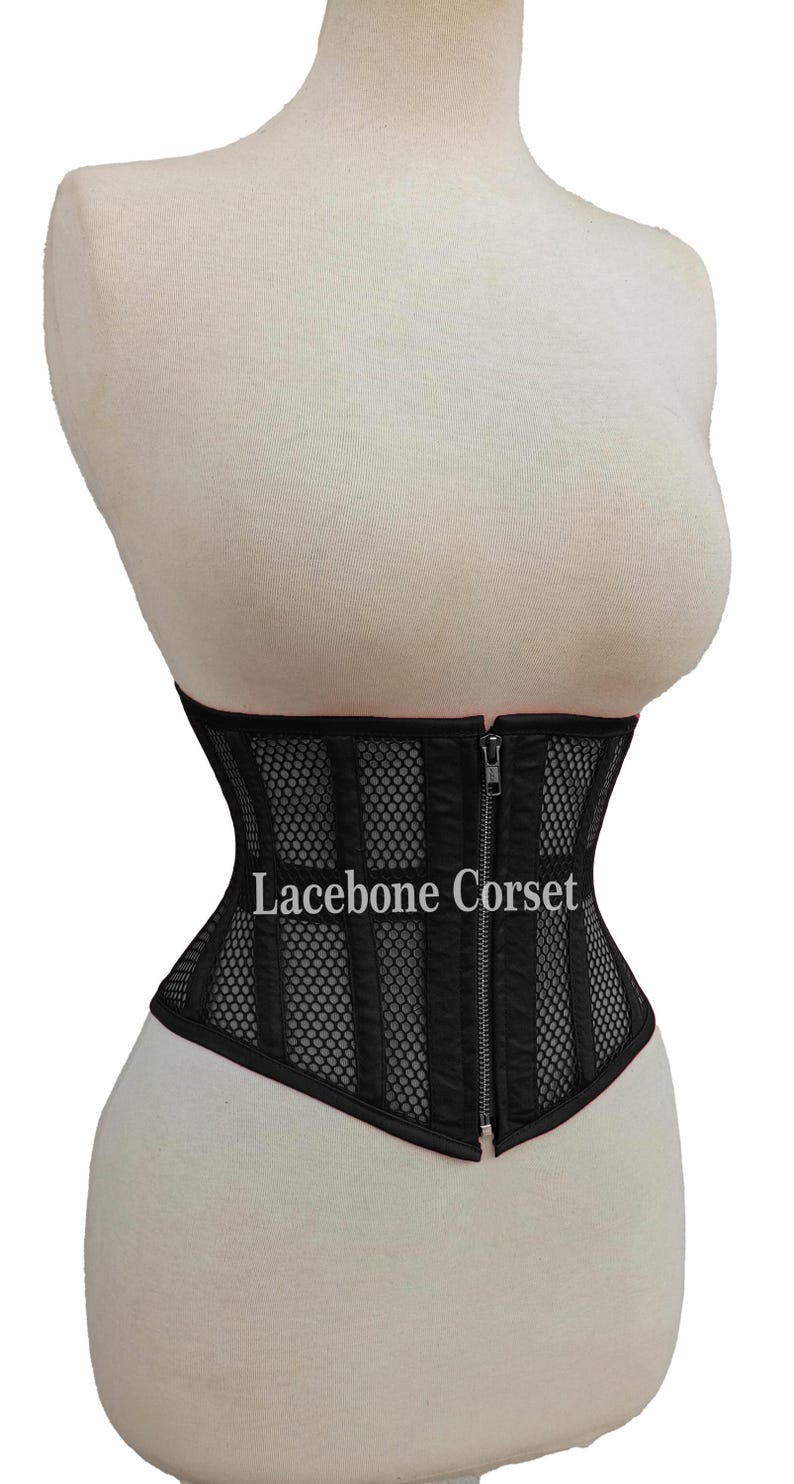 May include: Black corset with vertical panel design and mesh detailing. The corset features a front zipper closure and the text "Lacebone Corset". The garment is displayed on a mannequin.