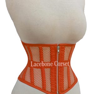 May include: Orange corset with a mesh and vertical stripe design, featuring a front zipper closure. The text "Lacebone Corset" is visible on the front. The corset is displayed on a mannequin.