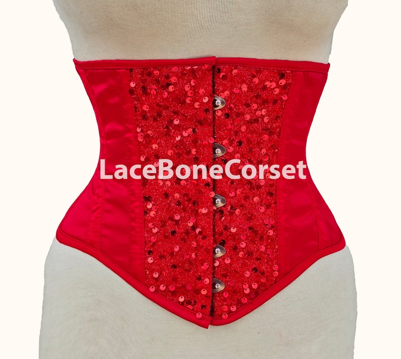 May include: Red satin corset with a red sequin design and a lace-up back. The corset has a metal busk closure and is decorated with the text "LaceBoneCorset".