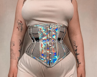 May include: A silver holographic corset with black mesh panels and a lace-up back. The corset has a busk closure and is worn over a white tank top.