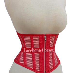 May include: Red corset with a mesh and vertical panel design, featuring a front zipper closure. The corset is displayed on a mannequin. The text "Lacebone Corset" is visible on the front.