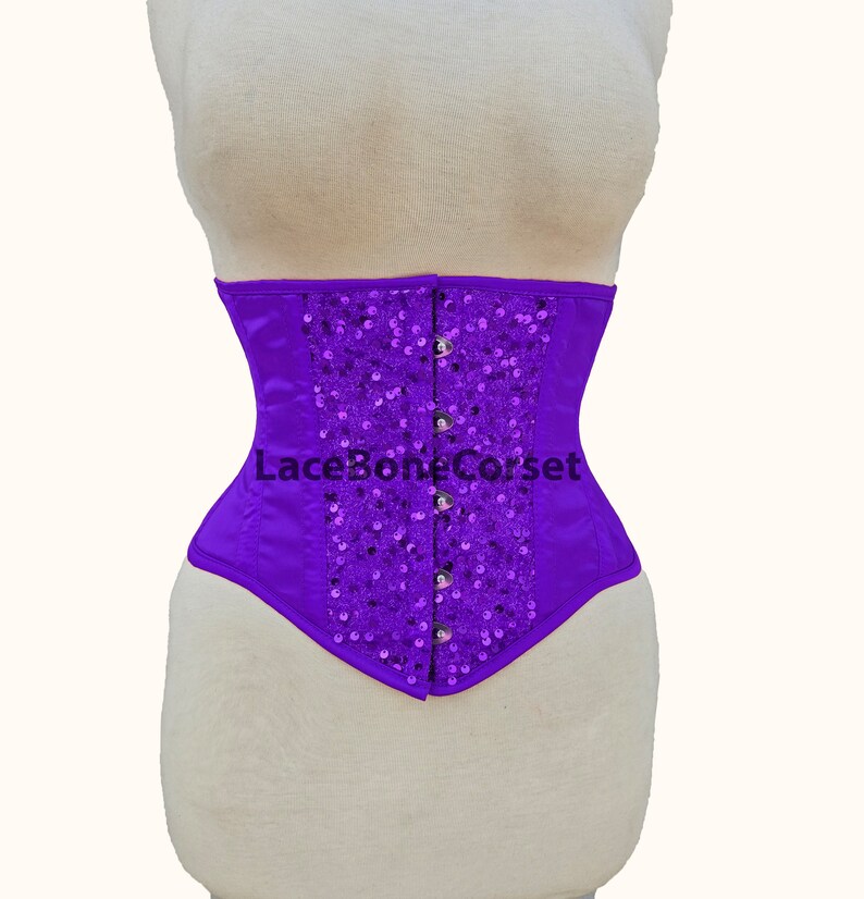 May include: Purple satin corset with a sequined design and a lace-up back. The corset has a boned structure and is designed to cinch the waist.