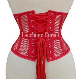 May include: Red corset with a mesh design and lace-up back. The corset has a structured shape and features the text "Lacebone Corset". The garment is displayed on a mannequin.