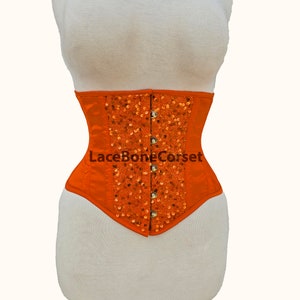 May include: Orange satin corset with a front panel of sequins and a lace-up back. The corset has a metal busk closure and is labeled "LaceBoneCorset".