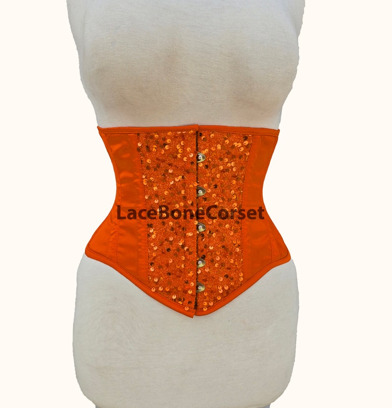 May include: Orange satin corset with a front panel of sequins and a lace-up back. The corset has a metal busk closure and is labeled "LaceBoneCorset".