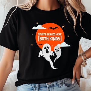 May include: Black t-shirt with a Halloween-themed graphic. The design features a large orange circle with bats, clouds, and stars. The text "SPIRITS SERVED HERE [BOTH KINDS]" is above two white ghost illustrations.