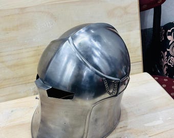 May include: A silver helmet with a chainmail chin strap. The helmet has a pointed top and a visor with a small opening for the eyes.