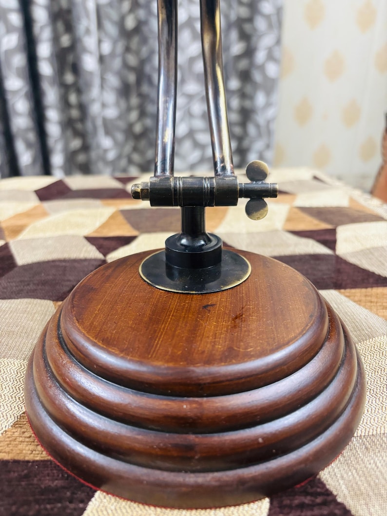 May include: A wooden base with three tiers, topped with a black metal base and a brass adjustable arm. The arm has a brass knob and a brass wing nut.